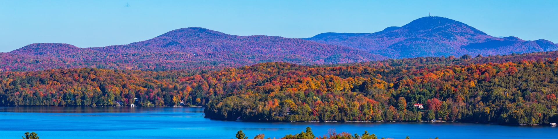 A lake surrounded by autumn-colored forests and distant mountains.
