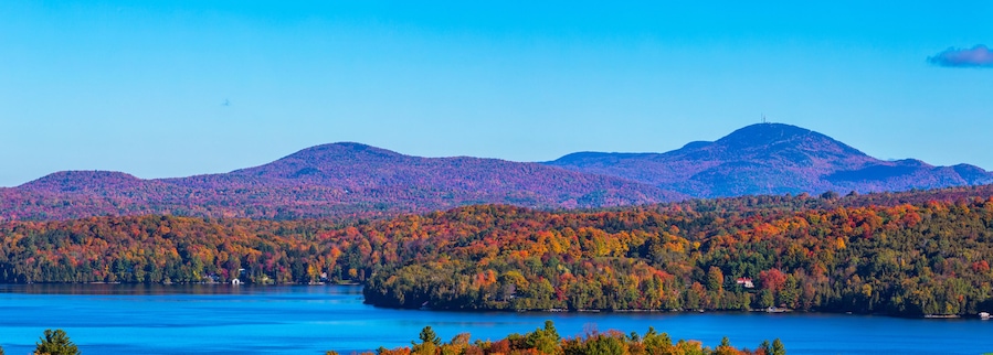 Un lac entouré de forêts aux couleurs automnales et de montagnes lointaines.
