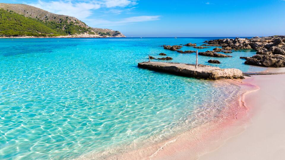 A clear turquoise sea, a sandy beach, and rocky outcrops.