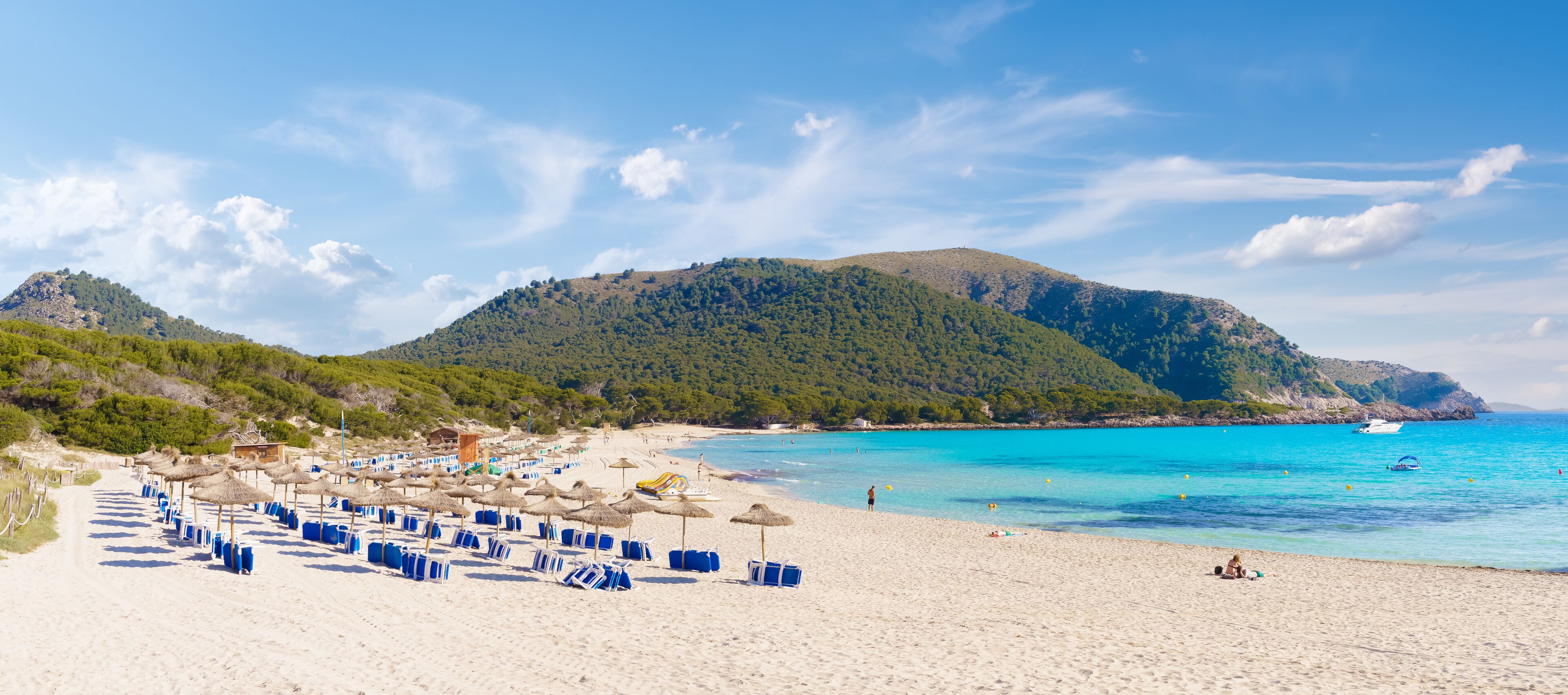 A beach with umbrellas, a clear blue sea, and a mountain in the background.