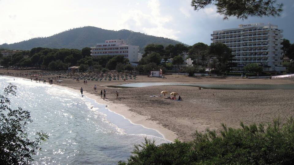 A beach with people, umbrellas, and buildings in the background.
