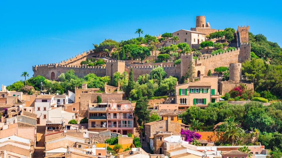 A historic walled city with medieval architecture, lush greenery, and terraced buildings.