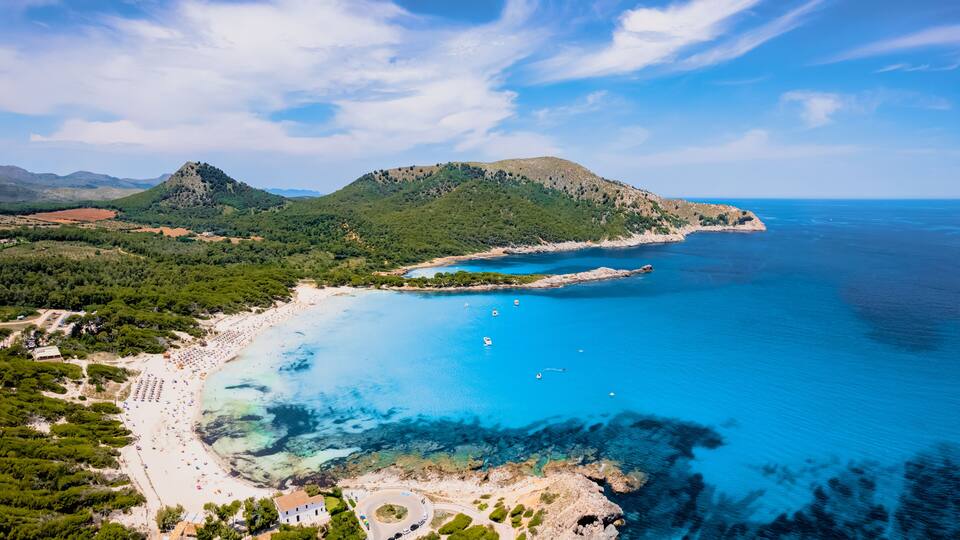 A coastal landscape with a beach, clear blue waters, and a mountainous backdrop.