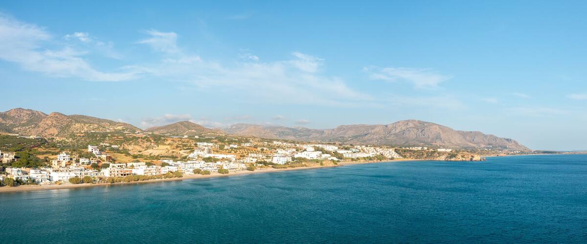 A coastal town with white buildings, a sandy beach, and mountains in the background.