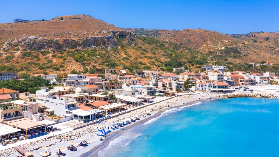 A coastal town with a beach, buildings, and a hilly landscape.
