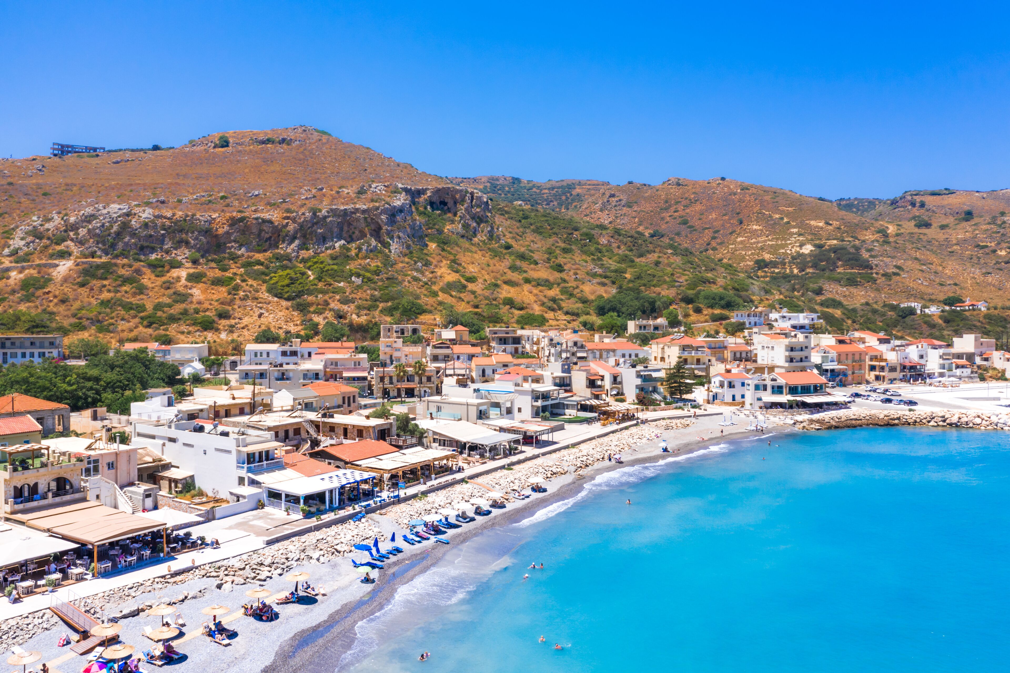 A coastal town with a beach, buildings, and a hilly landscape.