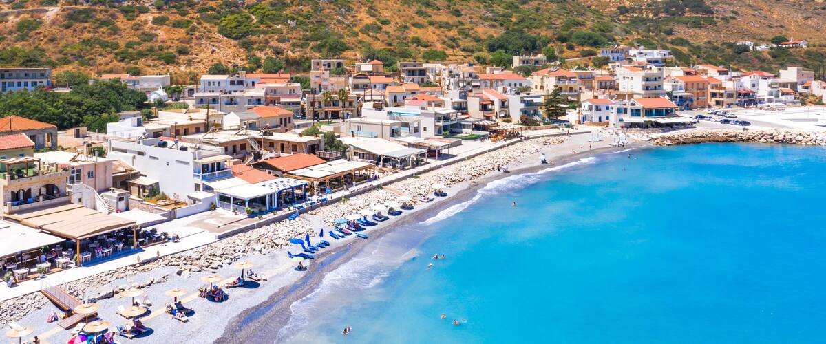 A coastal town with a beach, buildings, and a hilly landscape.