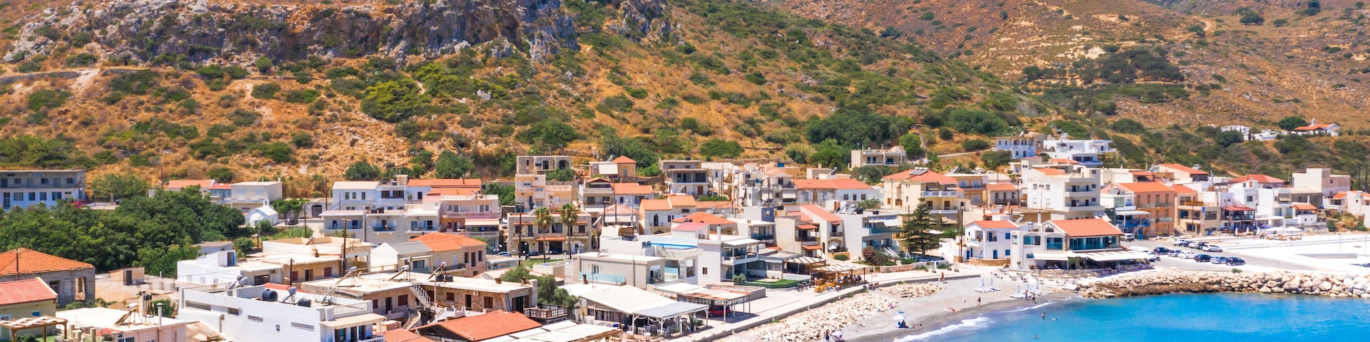A coastal town with a beach, buildings, and a hilly landscape.