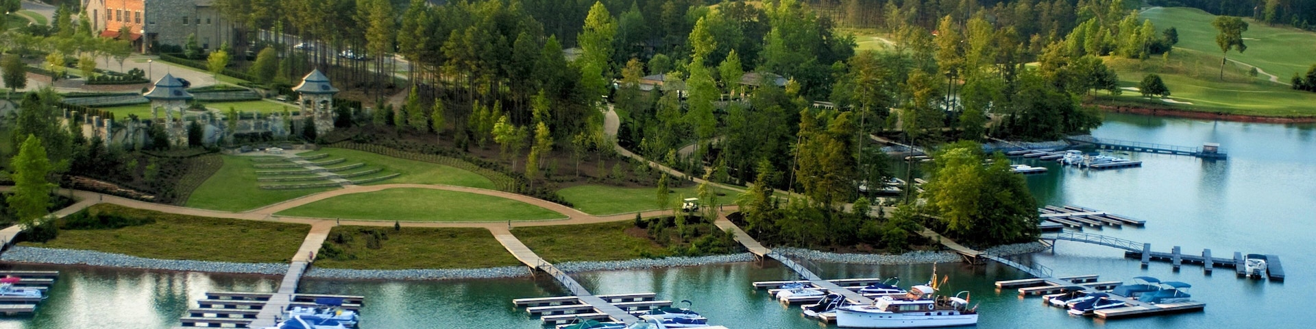 Ein Yachthafen am See mit vertäuten Booten, umgeben von üppiger Vegetation und einem Golfplatz.