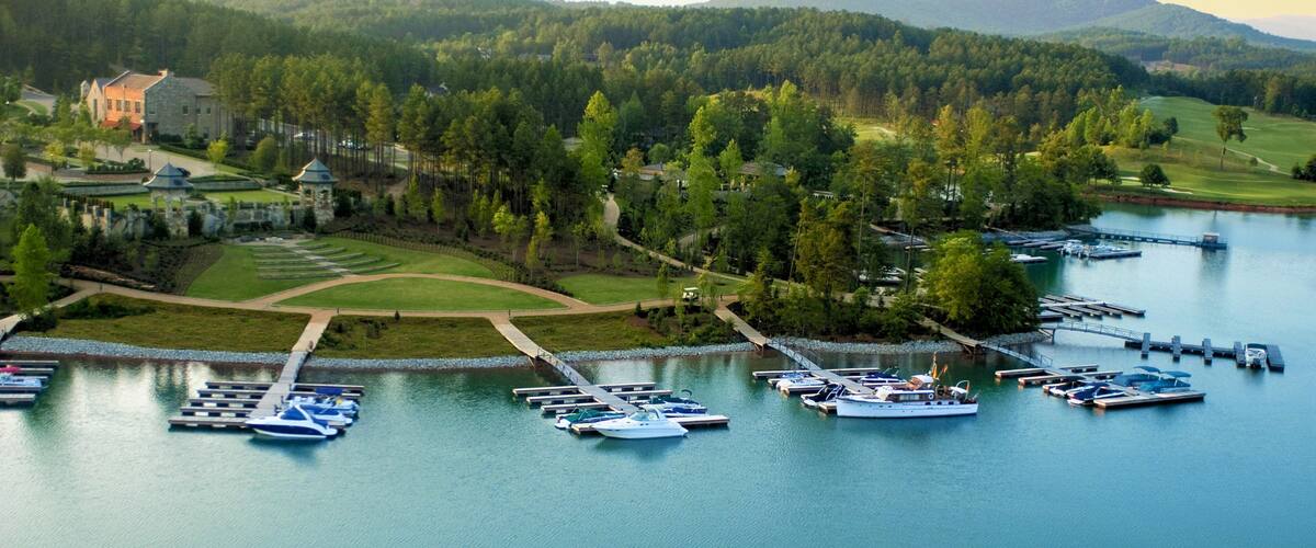 A lakeside marina with boats docked, surrounded by lush greenery and a golf course.