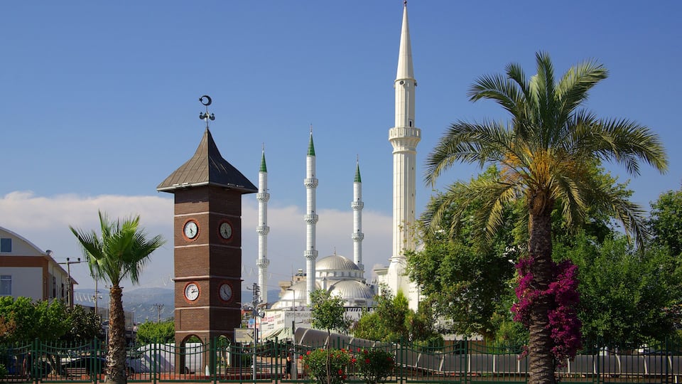 A mosque with minarets and a clock tower, surrounded by palm trees and a clear sky.