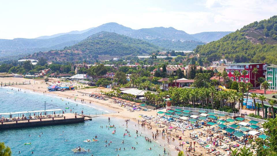 A coastal town with a beach, swimming area, and mountains in the background.