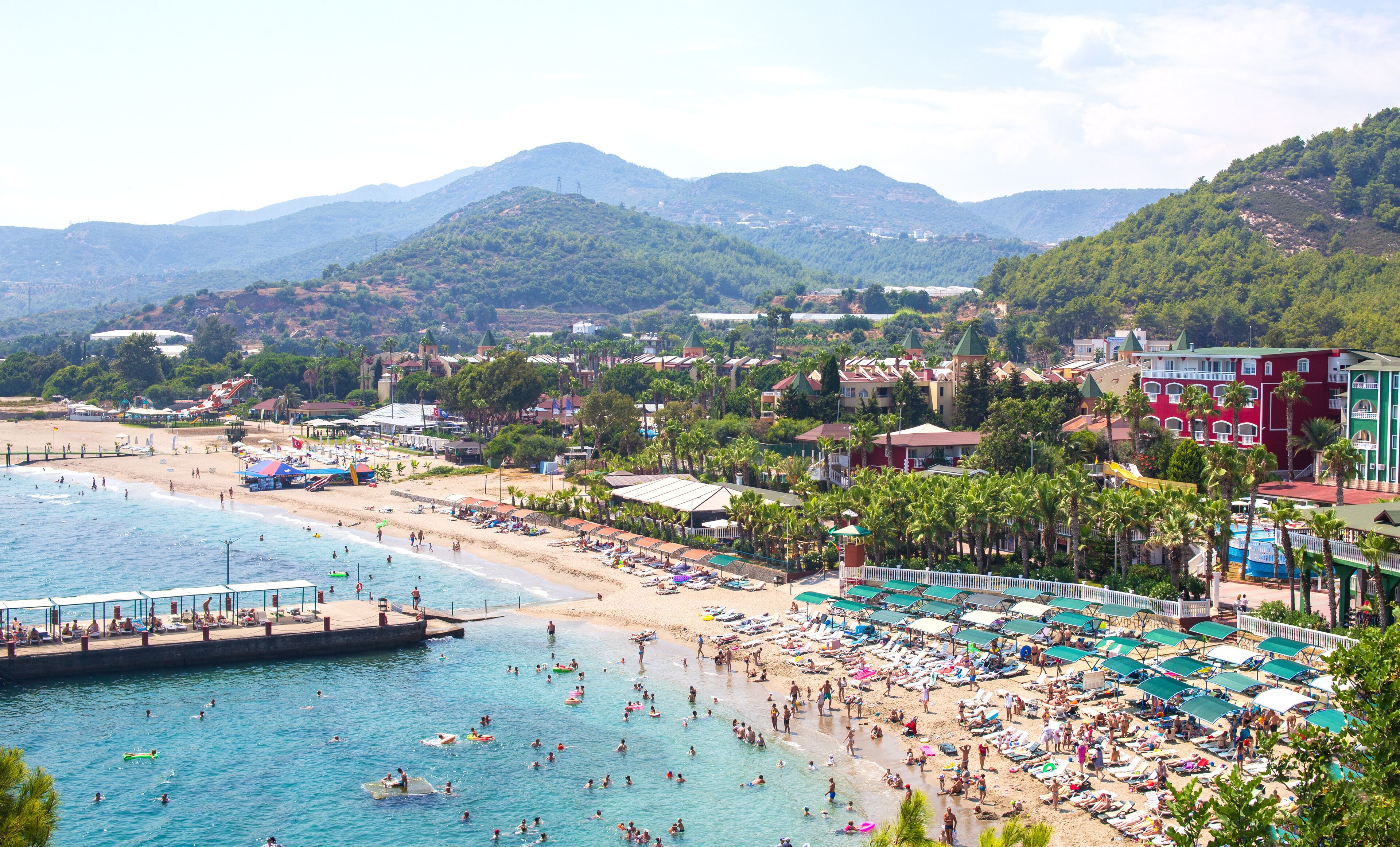 A coastal town with a beach, swimming area, and mountains in the background.