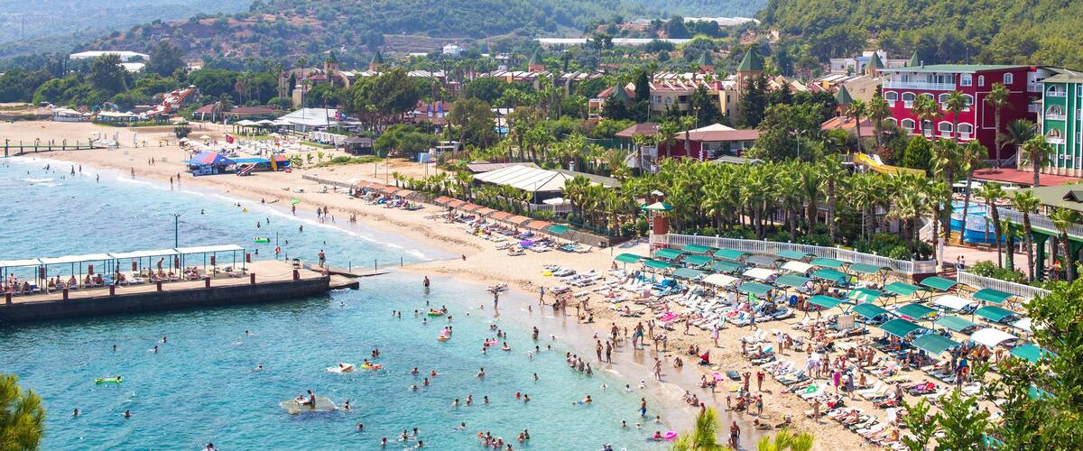 A coastal town with a beach, swimming area, and mountains in the background.