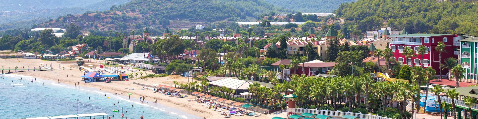A coastal town with a beach, swimming area, and mountains in the background.
