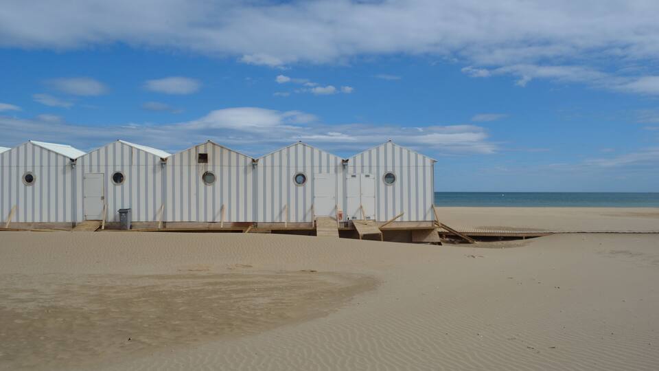 A row of beach huts with a sandy beach and ocean in the background.