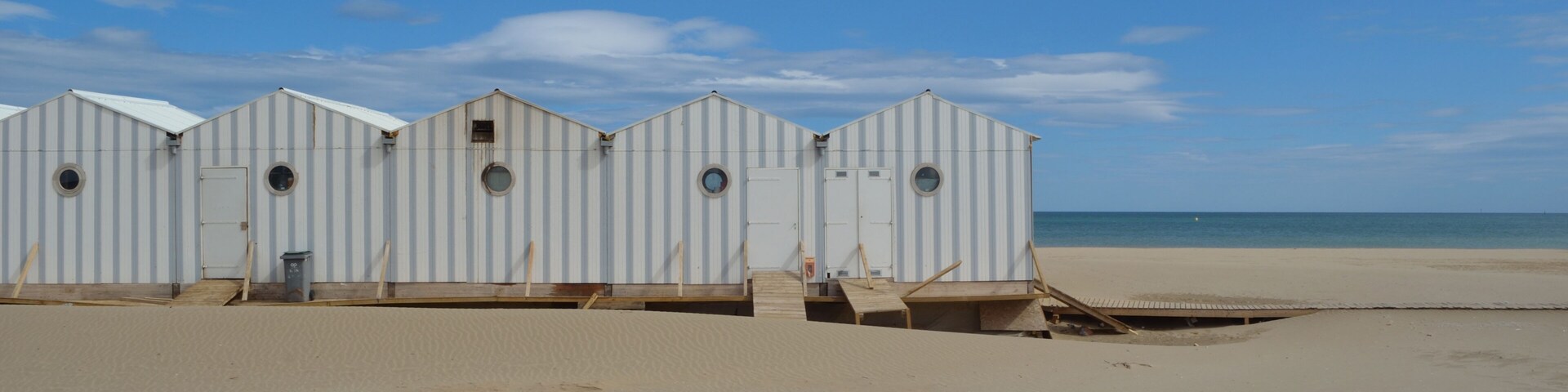 Eine Reihe von Strandhäusern mit Sandstrand und dem Meer im Hintergrund.