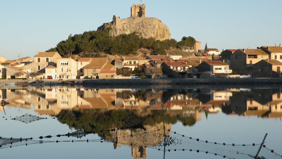 A coastal town with a prominent castle on a hill, reflecting in calm waters.