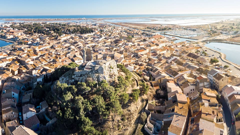 A coastal town with a dense cluster of buildings, a prominent rocky hill, and a marina.