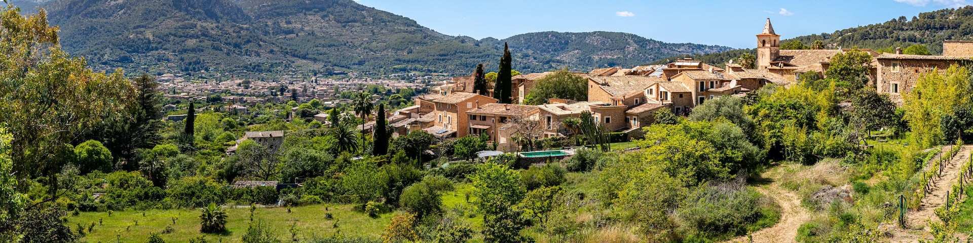 Panoramic view over the quaint village Biniaraix, framed by the lush valley of Sóller and Serra de Tramuntana mountains on a sunny day, ideal for promoting Mallorca as a tranquil travel destination.