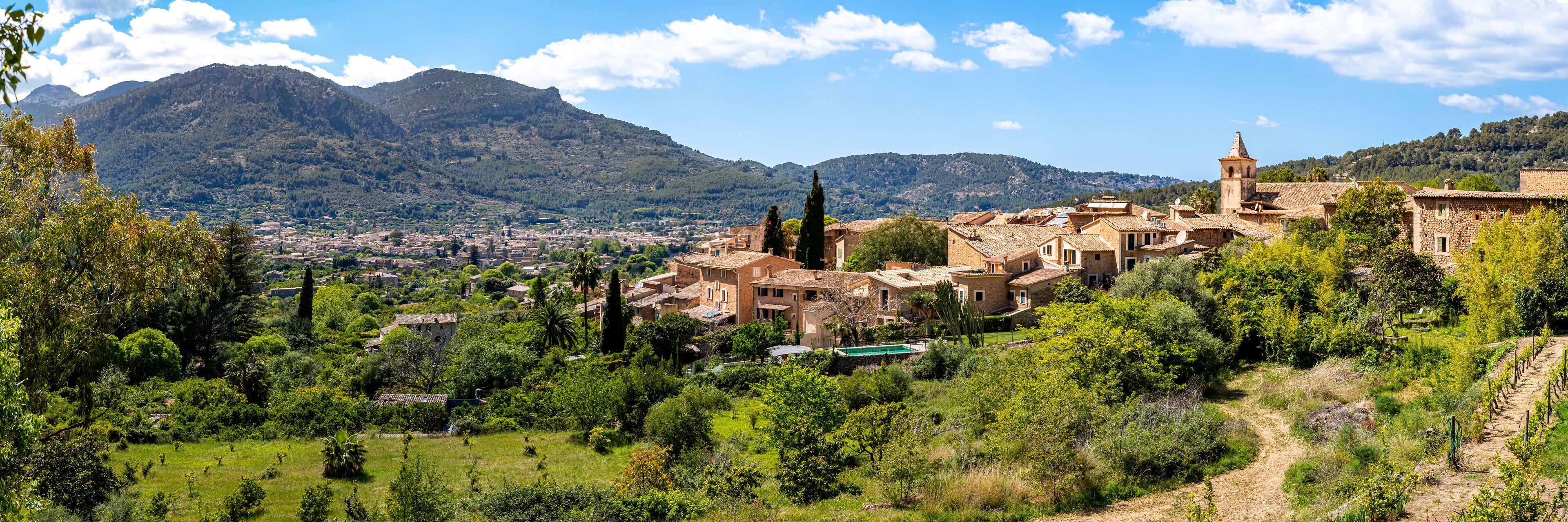 Panoramic view over the quaint village Biniaraix, framed by the lush valley of Sóller and Serra de Tramuntana mountains on a sunny day, ideal for promoting Mallorca as a tranquil travel destination.