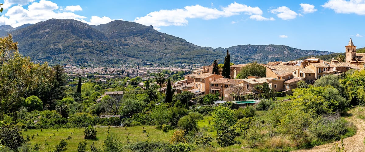 Panoramic view over the quaint village Biniaraix, framed by the lush valley of Sóller and Serra de Tramuntana mountains on a sunny day, ideal for promoting Mallorca as a tranquil travel destination.