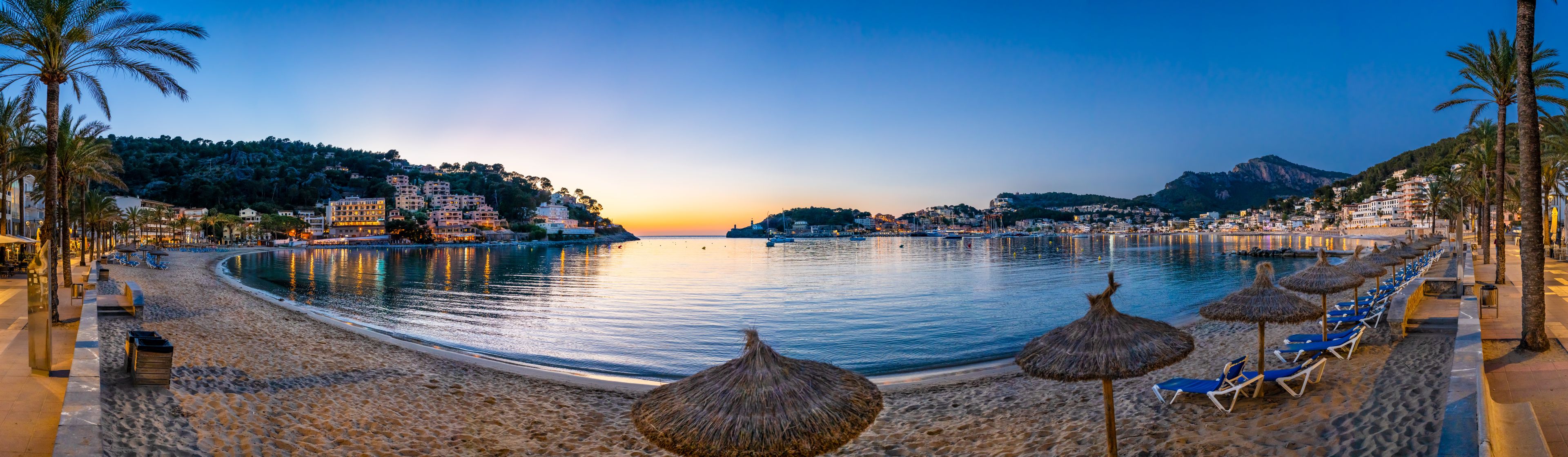 A beach with palm trees, beach umbrellas, and a calm sea at sunset.