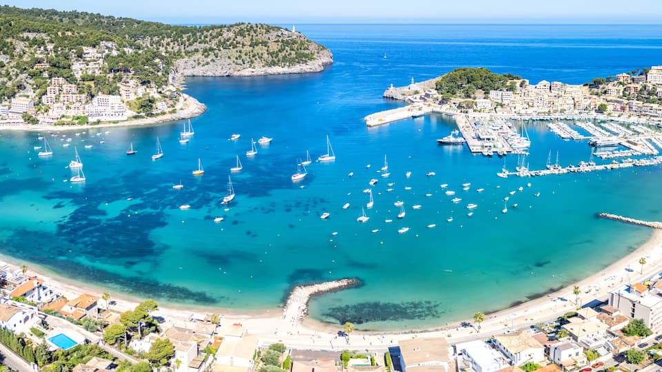 A coastal town with a marina, clear blue waters, and a hilly backdrop.