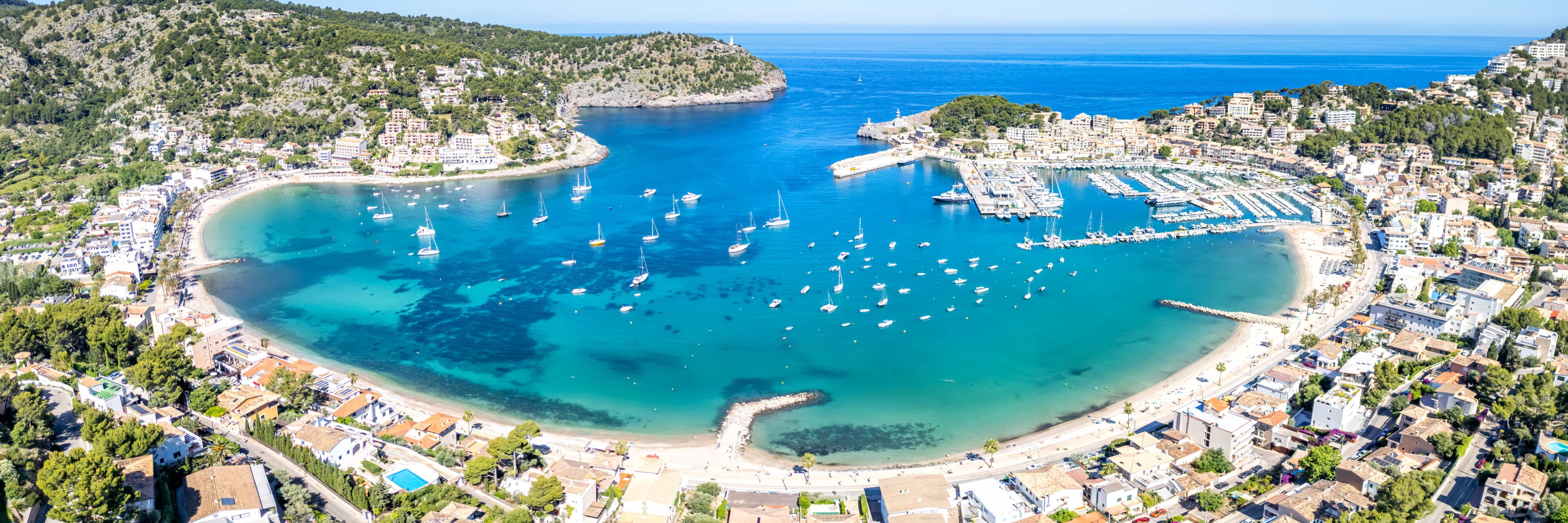 A coastal town with a marina, clear blue waters, and a hilly backdrop.