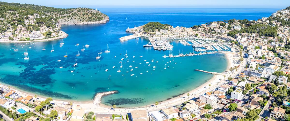A coastal town with a marina, clear blue waters, and a hilly backdrop.