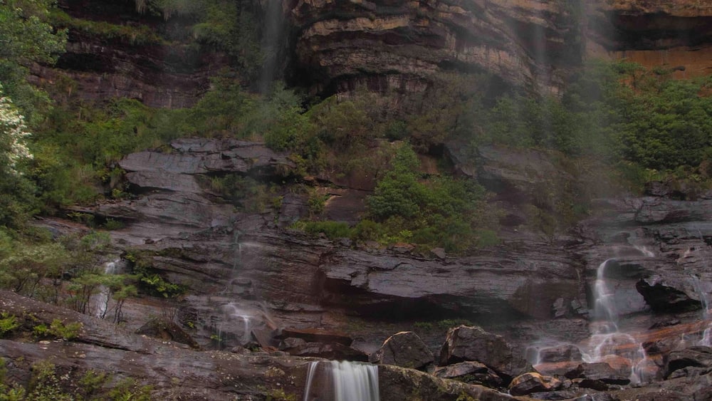 Ein Wasserfall stürzt über eine felsige Klippe, darunter üppige Vegetation.