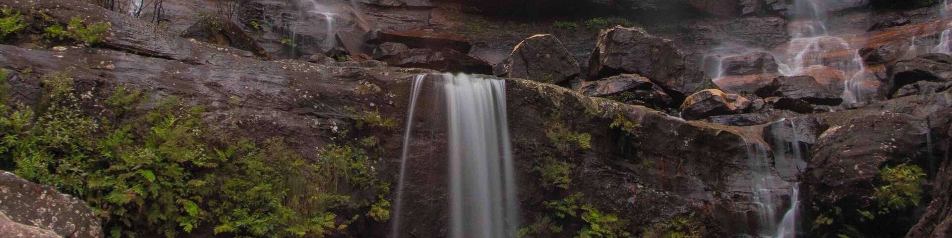A waterfall cascading down a rocky cliff with lush greenery at its base.