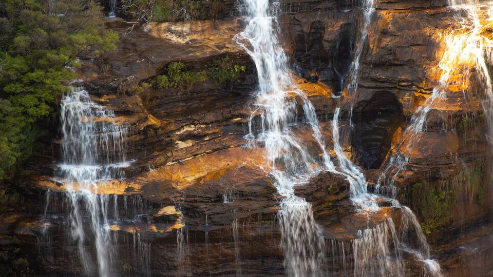 A multi-tiered waterfall cascading over rocky terrain with lush greenery.