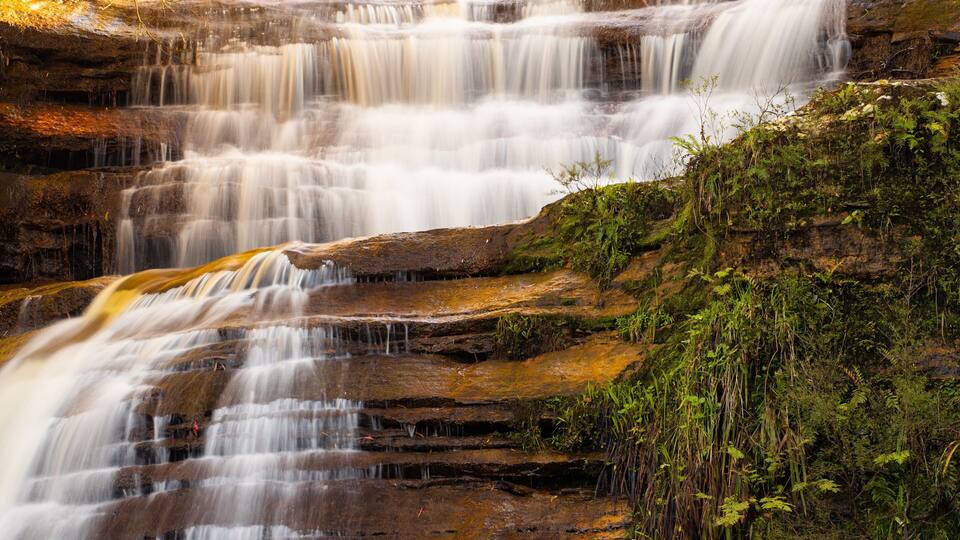 A multi-tiered waterfall cascading over rocky terrain with lush greenery.