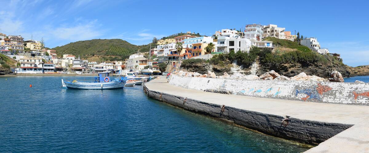A coastal town with colorful buildings, a rocky shoreline, and boats docked at the harbor.