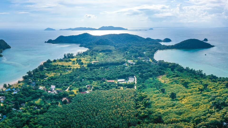 An aerial view of a tropical island with clear turquoise waters, lush greenery, and scattered houses.