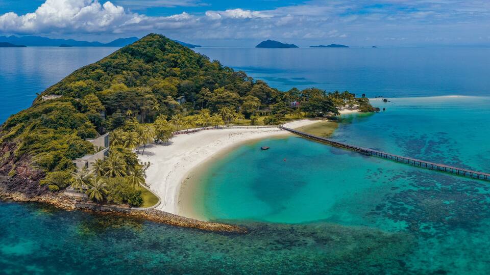 An island with a white sandy beach, clear turquoise waters, and a pier extending into the sea.