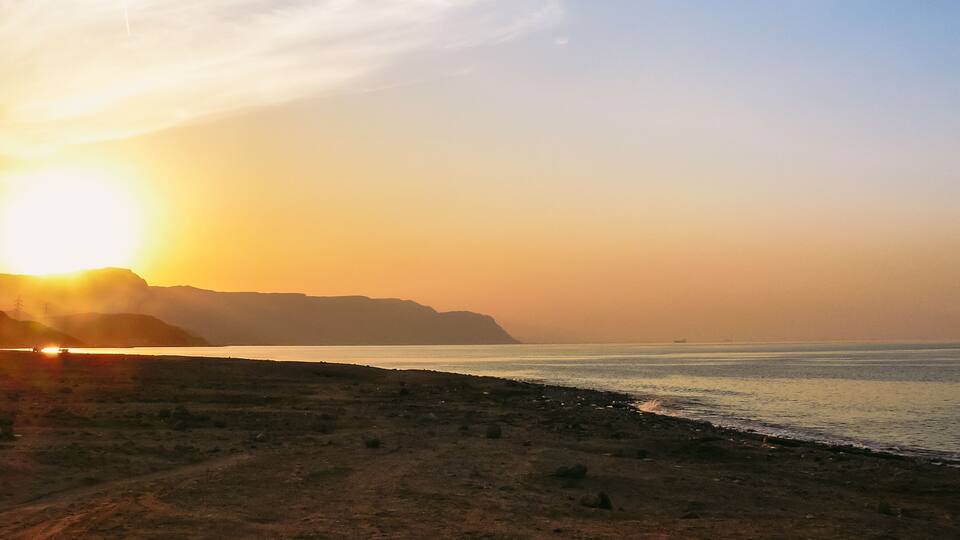A sunset over a beach with a distant mountain range.