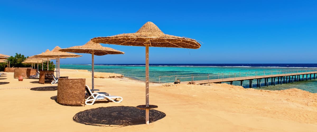 A beach with thatched umbrellas, lounge chairs, and a wooden pier extending into the sea.