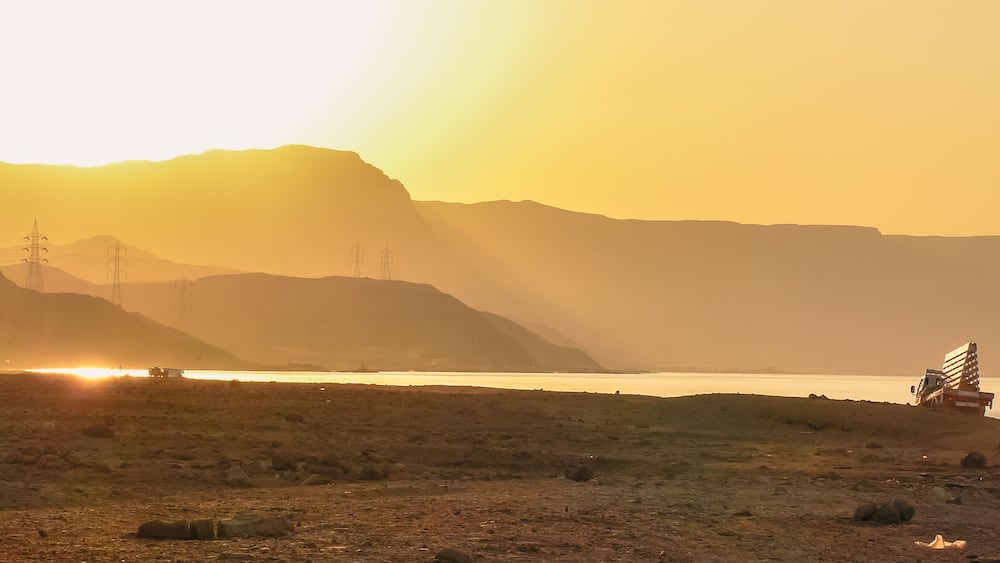 Sunset at Al Ain Al Sokhna, Suez, Egypt, with a truck driving along the beach. Mountains and soft sunlight create a tranquil backdrop