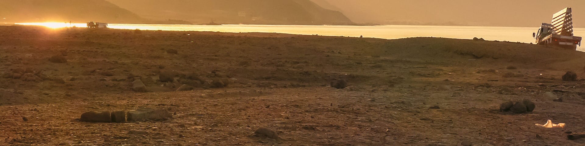 Sunset at Al Ain Al Sokhna, Suez, Egypt, with a truck driving along the beach. Mountains and soft sunlight create a tranquil backdrop