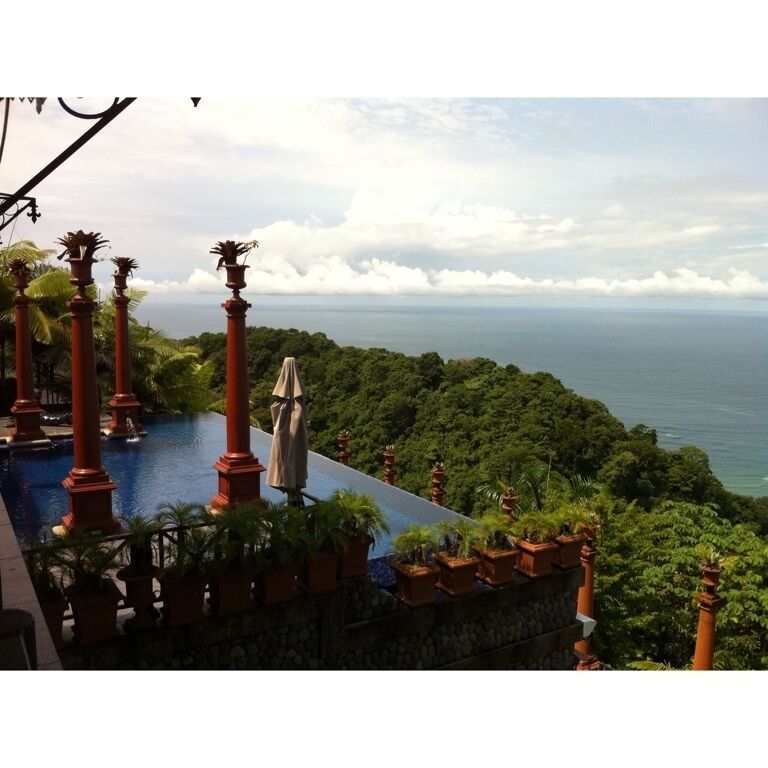 A tropical resort with a swimming pool, red pillars, and a view of the ocean.