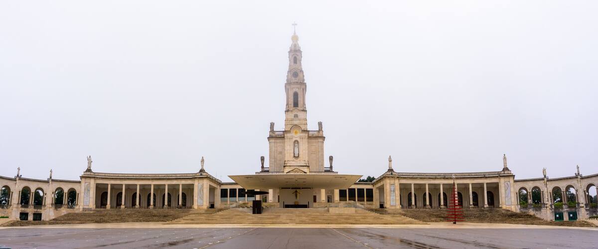 A large, historic building with a tall tower and a large open plaza in front.