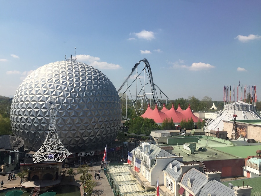 A large geodesic dome, a roller coaster, and a building with a red roof.