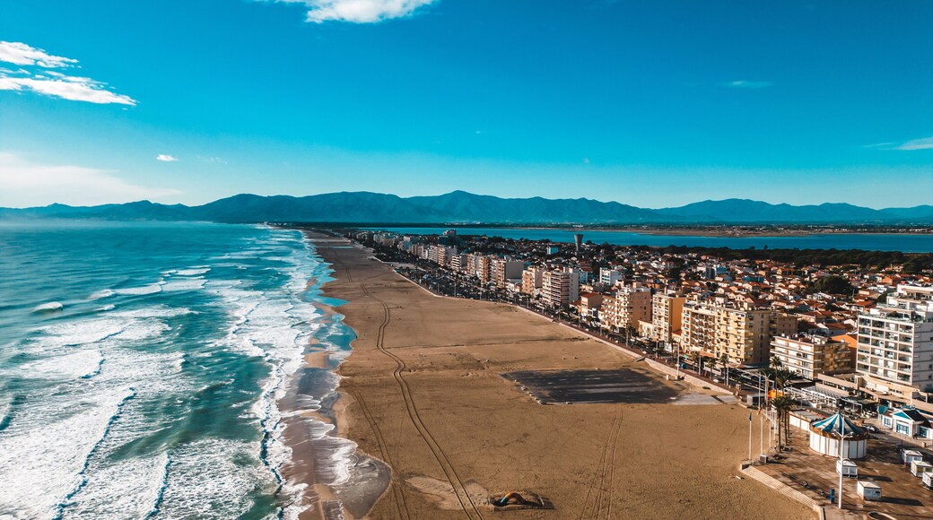 Aerial view of the beach meeting the urban landscape under a bright blue sky, a symphony of sand, sea, and city, Canet-en-Roussillon, Occitanie, France.