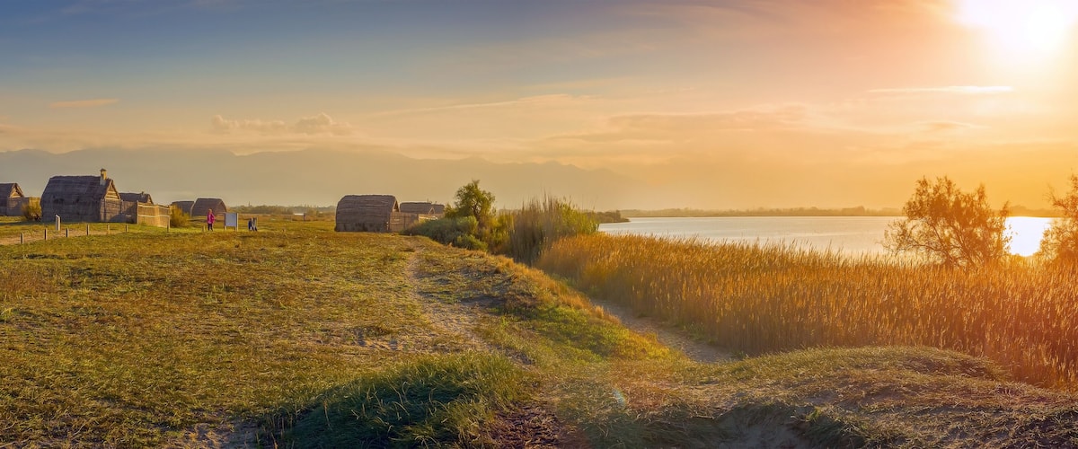 A rural landscape with traditional houses, a river, and mountains in the background.