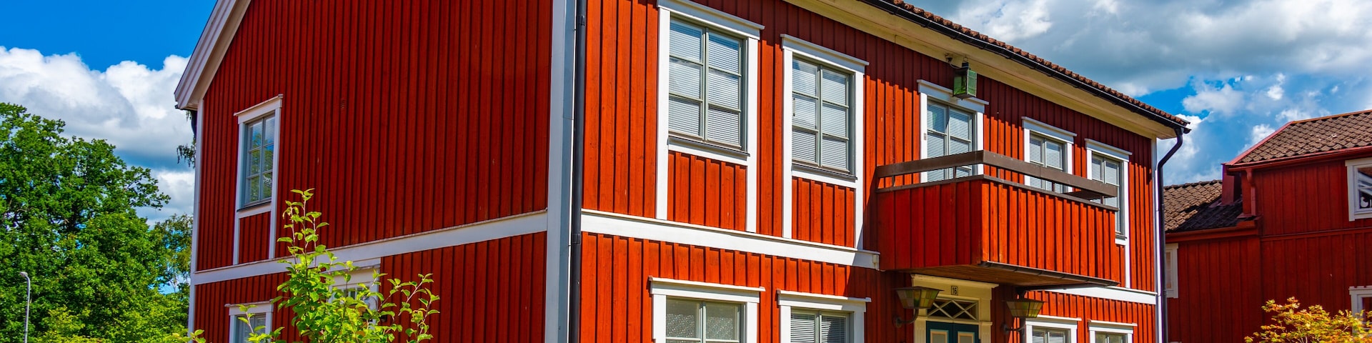 Una casa roja de dos pisos con detalles blancos, una puerta azul y un pequeño jardín con un banco.
