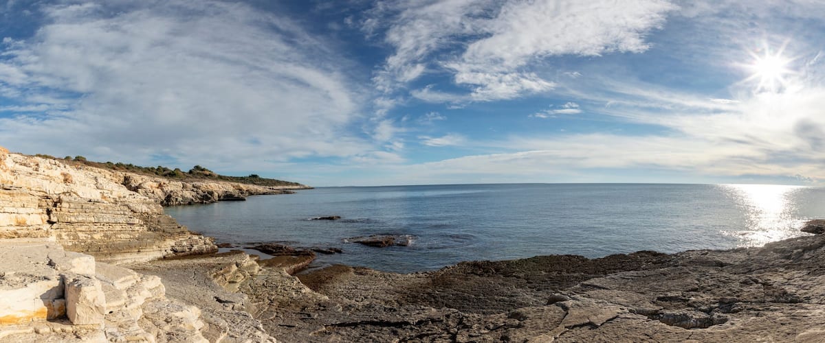A coastal landscape with rocky cliffs, calm sea, and a clear sky.