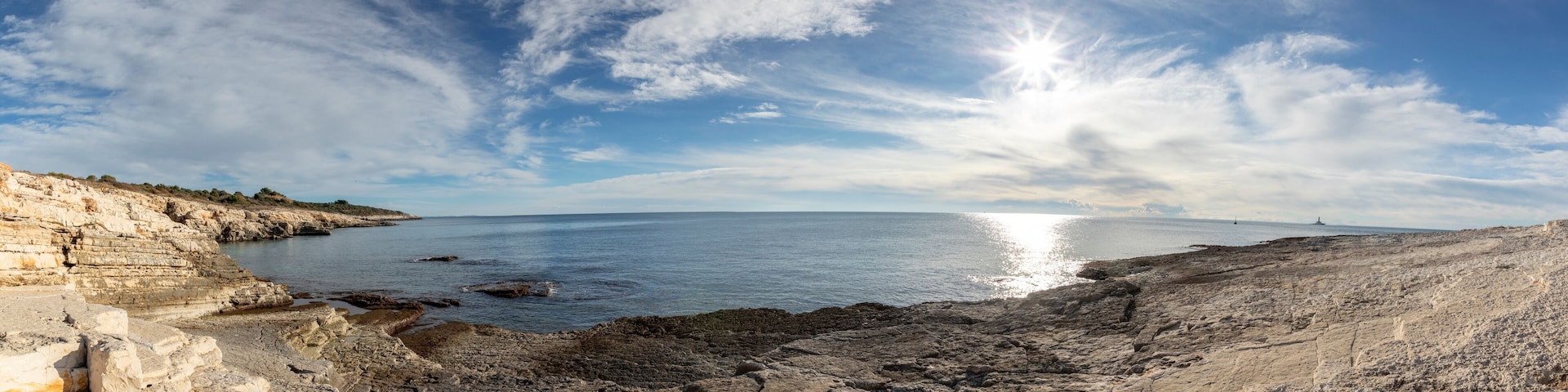 A coastal landscape with rocky cliffs, calm sea, and a clear sky.