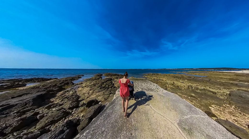 Eine Frau im roten Kleid geht auf einem steinigen Weg zum Meer.